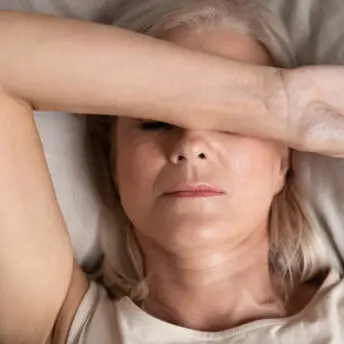 Close up top view middle-aged woman lying down in bed on pillow put hand on face, concept of female having insomnia sleeping disorder or migraine pain, melancholic mood, personal life troubles concept